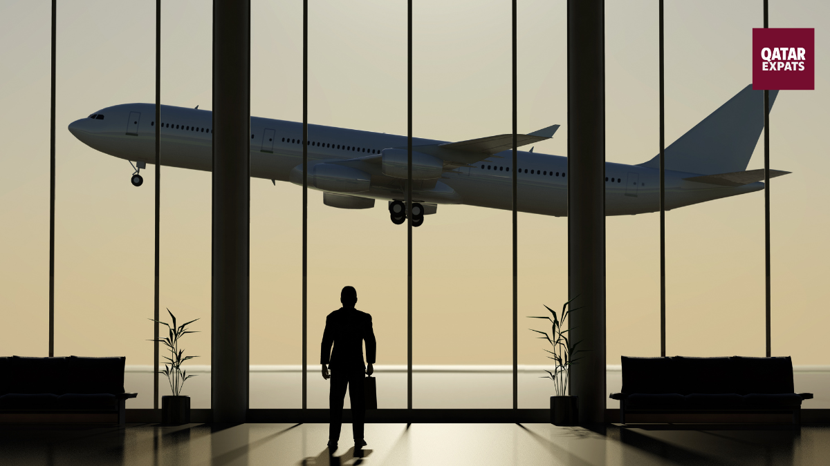 Silhouette of a traveller standing in an airport terminal, watching a passenger airplane take off through large glass windows.