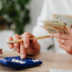 Person calculating expenses with cash and a calculator while preparing to send money internationally from Qatar.