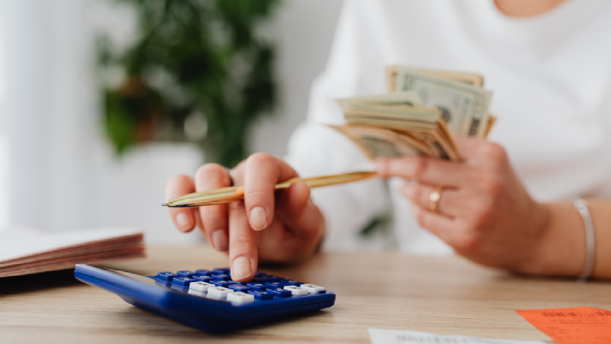 Person calculating expenses with cash and a calculator while preparing to send money internationally from Qatar.